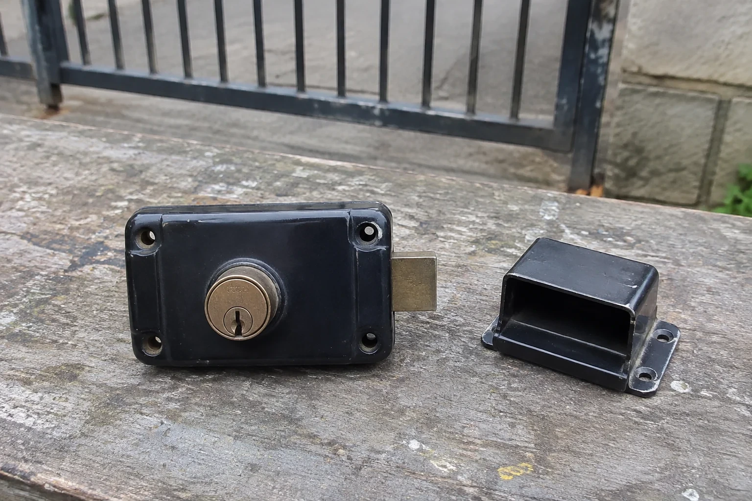 Detached rim gate lock and separate box keeper on an outdoor workbench.