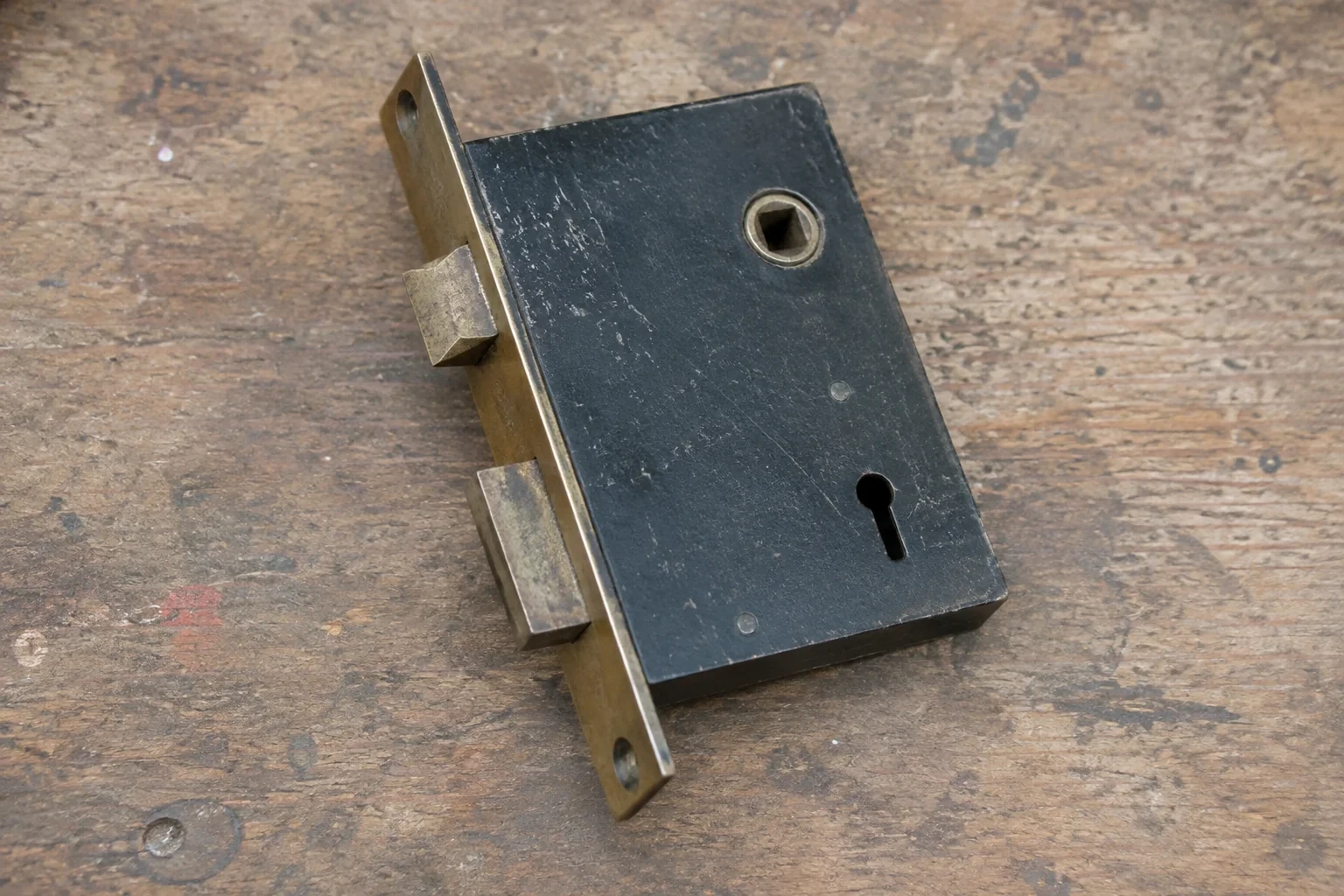 Closed mortise lock case with spindle opening, keyhole, latch and deadbolt on a wooden workbench.